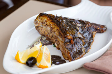 Fried fish flounder with lemon and black olives on a white plate