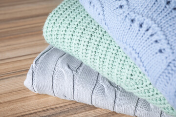 Stack of folded warm sweaters on wooden table, closeup
