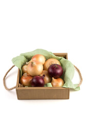 Onions of different varieties in a beautiful wooden packing box on a linen napkin, isolated on a white background, side view, vertical frame, Vegetable background. Concept of natural products.