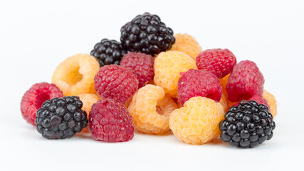 Lot of organic red and yellow raspberries and black blackberries on white background. Selective focus