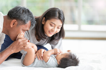 Portrait nice family on the bed in while living room and playing with their baby boy. Father, mother and one year old little son have fun together, Intimacy moment. Copy space.