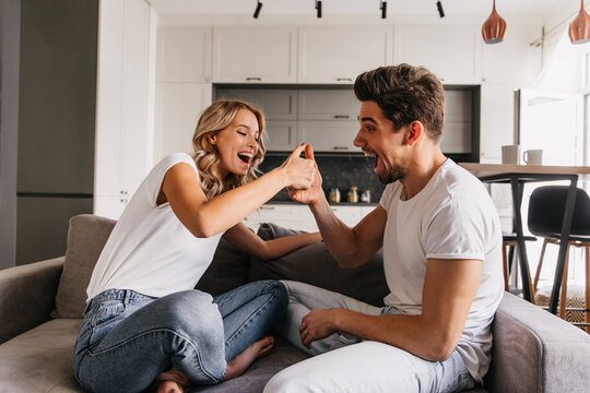 Two cheerful people sitting on sofa and playing on thumbs. Man looks surprised and his gilfriend looks very happy and ready to win.