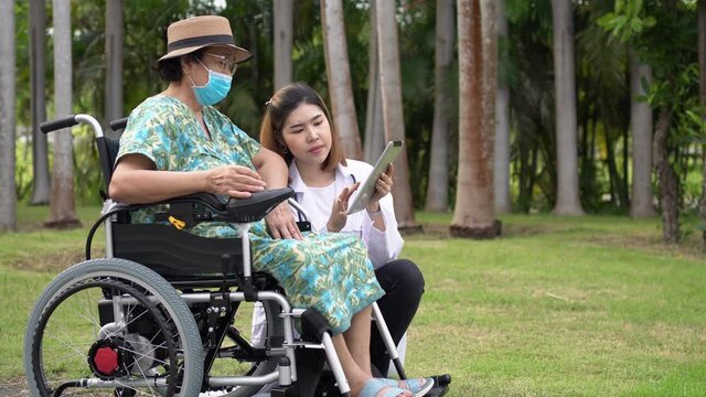 Doctor help and care Asian senior or elderly old lady woman patient sitting on wheelchair at park, Doctor with Senior patient use the electric wheelchair.