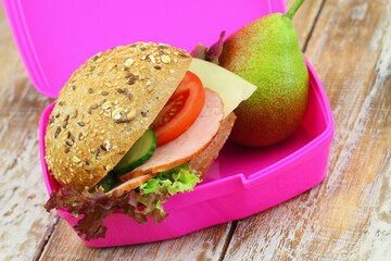 Healthy lunchbox containing whole grain roll with ham, lettuce, tomato and cucumber and sweet pear
