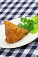 Indian samosa on green lettuce on white plate and fresh coriander leaves
