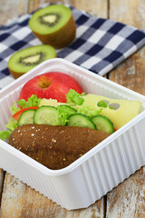 Healthy lunch box with whole grain roll with Swiss cheese, lettuce, tomato and cucumber, apple and kiwi fruit


