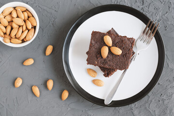 Traditional homemade chocolate brownie served on a plate with fork and almond nuts, top view