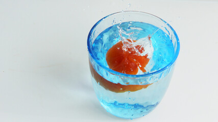 red cherries fall into a blue glass of water