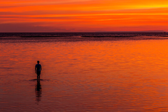 Silhouette of a man walking in the ocean at sunset