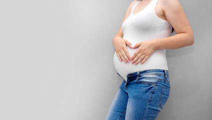 Pregnant woman holds hands on belly on a grey background. Pregnancy, maternity, preparation and expectation concept. Close-up, copy space. Beautiful tender mood photo of pregnancy.