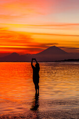 Person silhouetted taking a photo of volcano at sunset