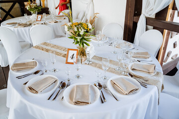 Serving a festive table, placing plates on the table, a Banquet table with a white tablecloth, preparing the dining table for the holiday, Cutlery is arranged according to etiquette. flowers 