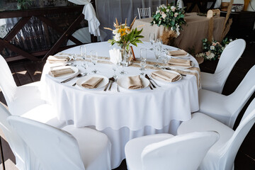 Serving a festive table, placing plates on the table, a Banquet table with a white tablecloth, preparing the dining table for the holiday, Cutlery is arranged according to etiquette. 