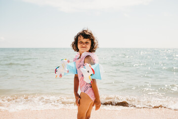 Toddler girl wearing pink swimsuit with unicorns and kids' swimming armbands on the sea