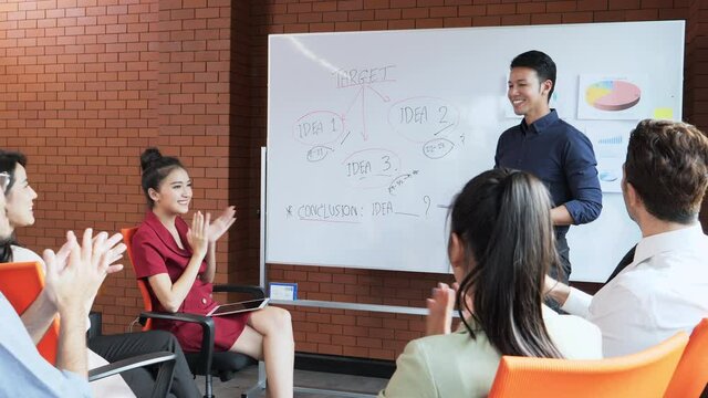 Business man are standing smart front of room presentation the topic of their work on a whiteboard in the meeting room. Everyone clapping for him.