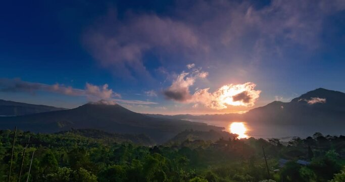 Time lapse of sunrise with view on volcanoes and lake. Clouds are moving quick in blue sky, the sun is rising