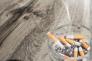 Ashtray and smoked cigarettes with smoke on desk