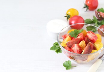 Vegetable salad of fresh yellow, red and black tomatoes with parsley in a glass bowl on a white background copy space 