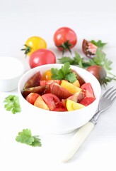 Vegetable salad of fresh yellow, red and black tomatoes with parsley in a bowl on a white background