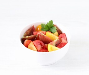 Vegetable salad of fresh yellow, red and black tomatoes with parsley in a bowl on a white background