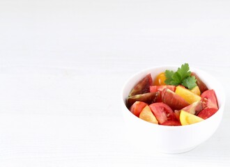 Vegetable salad of fresh yellow, red and black tomatoes with parsley in a bowl on a white background copy space