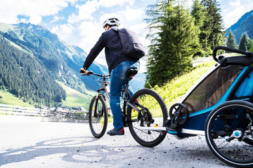 Obraz premium Man With E Bike MTB And Kid Trailer