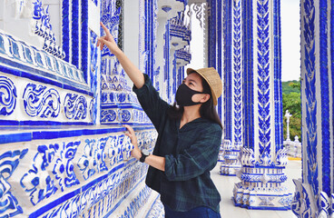 Traveller wearing masks enjoying a looking at sculpture on temple in Thailand.