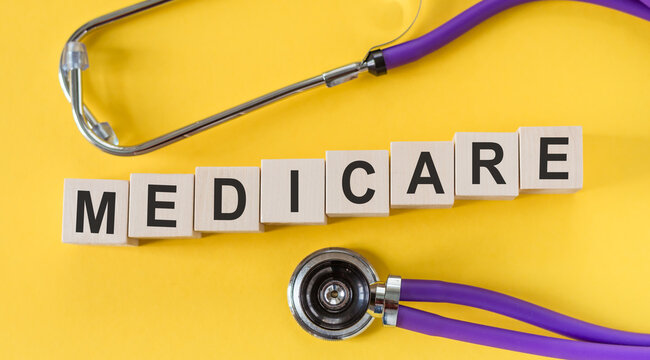 Medicare word written on cube shape wooden blocks on yellow table with stethoscope