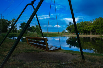 Swing for relaxation in an empty evening park by the lake at sunset