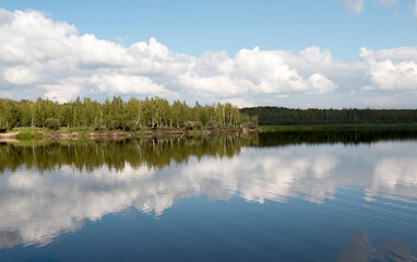 Forest lake view, smooth surface of a lake with clouds reflected, shining level of a forest lake