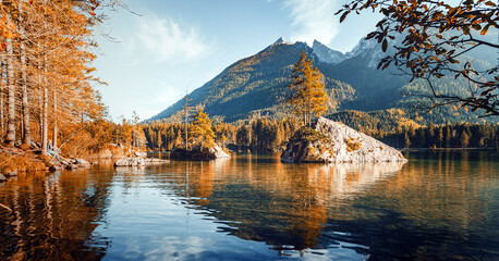 Fototapeta premium Amazing sunny landscape. Autumn nature scenery. Vivid morning. colorful forest on Hintersee lake with perfect sky and majestic mountains on background. Scenery of nature background for design