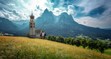 Fototapeta premium Splendid summer nature landscape. Panoramic view of idyllic mountain scenery in Alps with fresh green meadows in bloom on a beautiful sunny day in summer. famous San Valentino Church. Dolomite Alps