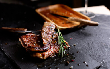 Pieces of Beef Steak on a dark plate with rosemary and pepper