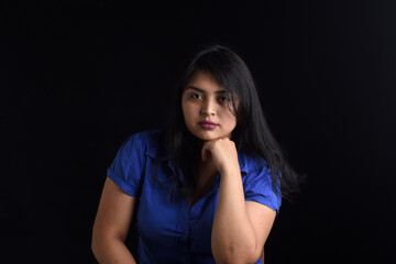 portrait of a latin woman sitting on chair and looking at camera on black background, hand on chin