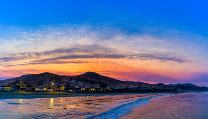 Panoramic sunrise over town, hills, beach, waves