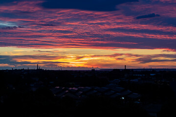 An aerial view of a beautiful colorful yellow, orange, pink blue sunset over an industrial city with rooftops 