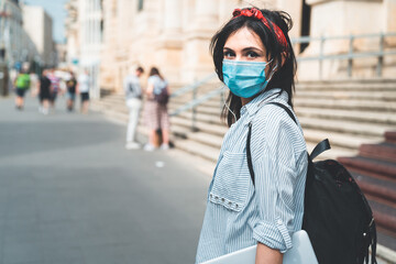 Back to School. Female student wearing protective face mask looking at camera while walking around university campus during COVID 19. Education, healthcare and pandemic concept