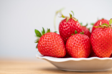 Lots of fresh strawberry berries in a white plate on a wooden table