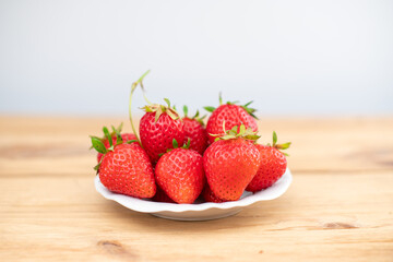 Lots of fresh strawberry berries in a white plate on a wooden table