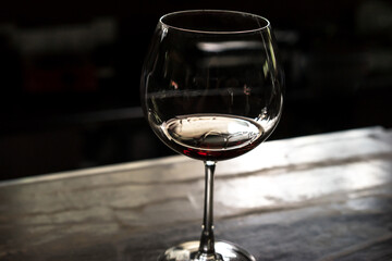 glass of red wine on the wooden table, dark blurred background, soft focus