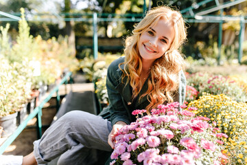 Against background of bright flowering plants and green bushes that grow in garden beautiful blonde...