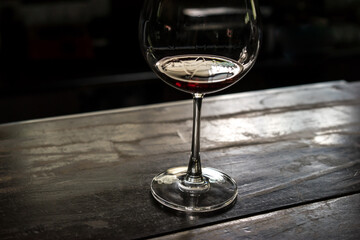 glass of red wine on the wooden table, dark blurred background, soft focus
