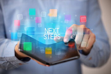 Young man holding a foldable smartphone with NEXT STEPS inscription, educational concept