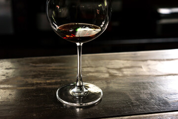 glass of red wine on the wooden table, dark blurred background, soft focus