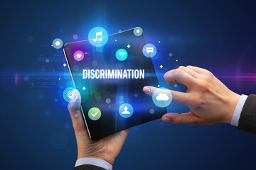 Businessman holding a foldable smartphone with DISCRIMINATION inscription, social media concept