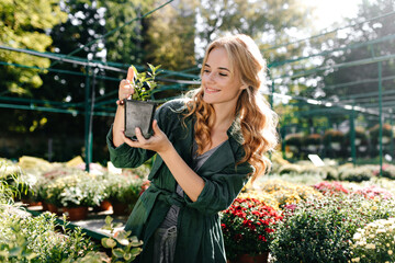 photo against background of plants and flowers in botanical garden. Beautiful blonde girl holds in...