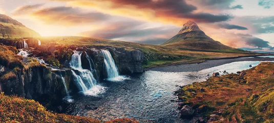 Fototapeten Erstaunliche Berglandschaft mit farbenfrohem, lebendigem Sonnenuntergang am bewölkten Himmel über dem berühmten Wasserfall Kirkjufellsfoss und dem Berg Kirkjufell. Island. beliebter Standort für Landschaftsfotografen. © jenyateua
