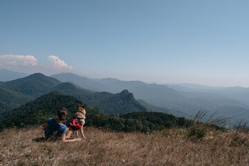Dog traveler goes to the mountains with his best friend man and enjoys nature and beautiful scenery. A young traveller girl is sitting on top of a mountain with her German shepherd.