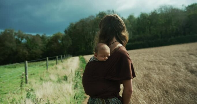 Mother with baby in sling standing in a field