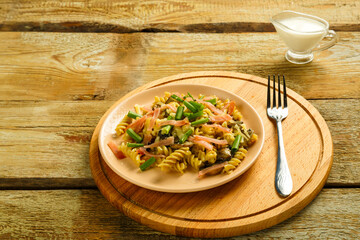 a plate with pasta with ham and mushrooms in a creamy sauce on a table with a fork on a round wooden stand.